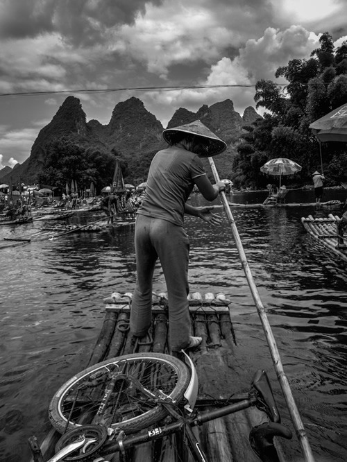 Woman in hat rowing basic boat with bike on it in Ladahk.