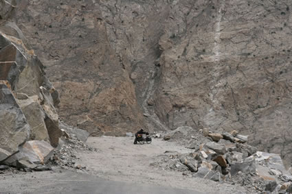 Insignificant forms on a bike seen against a massive cliff-face drop.