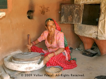 Woman seated and grinding grain with a wooden stick is a fine photo subject.