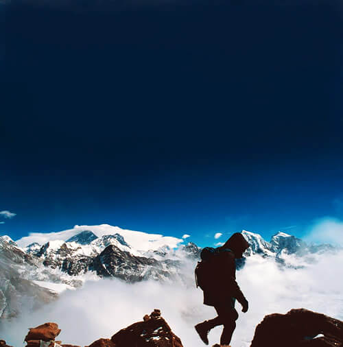 A trekker climbing the mountaintop in Nepal with the snow-capped Himalayas in the background.