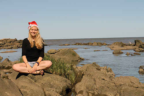 Author sitting on rocks near the ocean, enjoying the great weather during a Christmas that feels like summer.