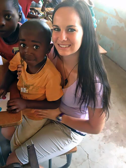 Marissa holding a small child on her lap in a classroom in Zambia.