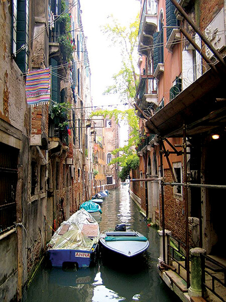 A narrow canal with boats moored in heart of Venice.